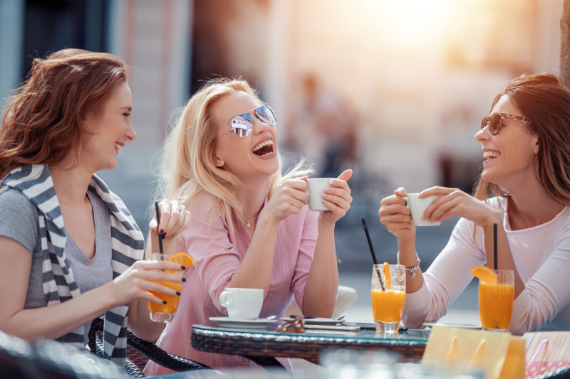 Women sitting at a coffee shop laughing  enjoying their time.